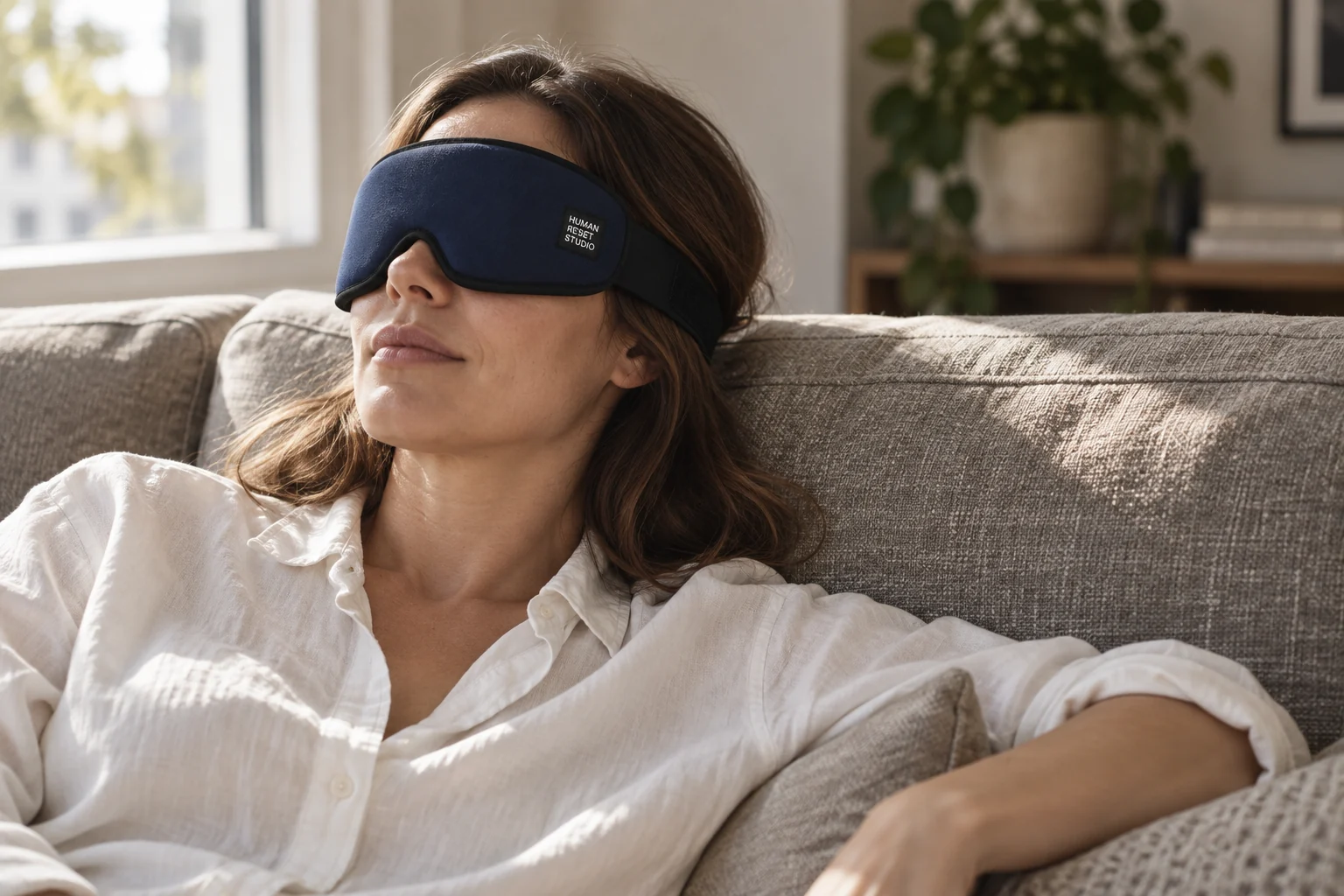 A woman resting on a linen sofa with a navy HRS eye wrap